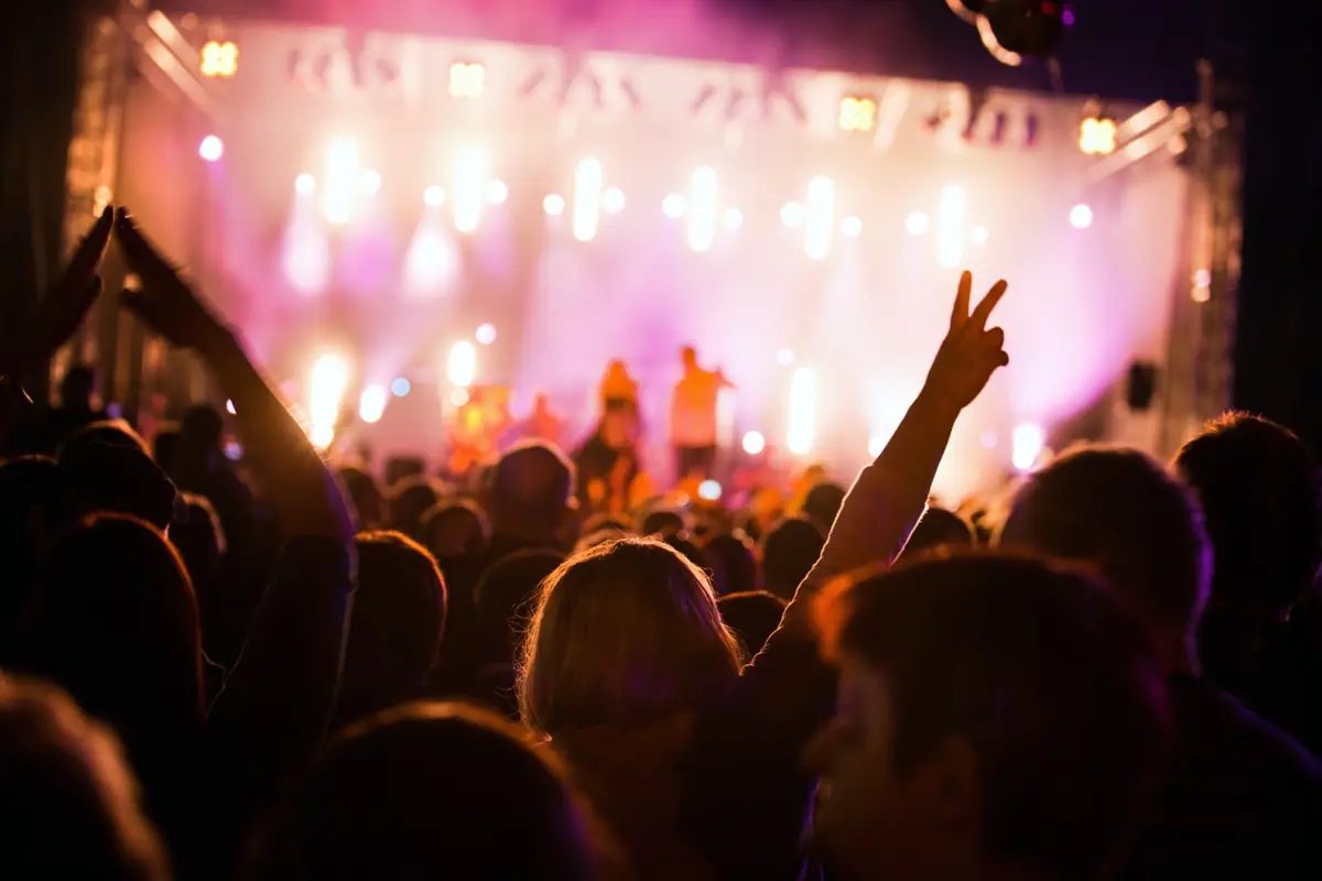 Público em um show com o palco iluminado ao fundo
